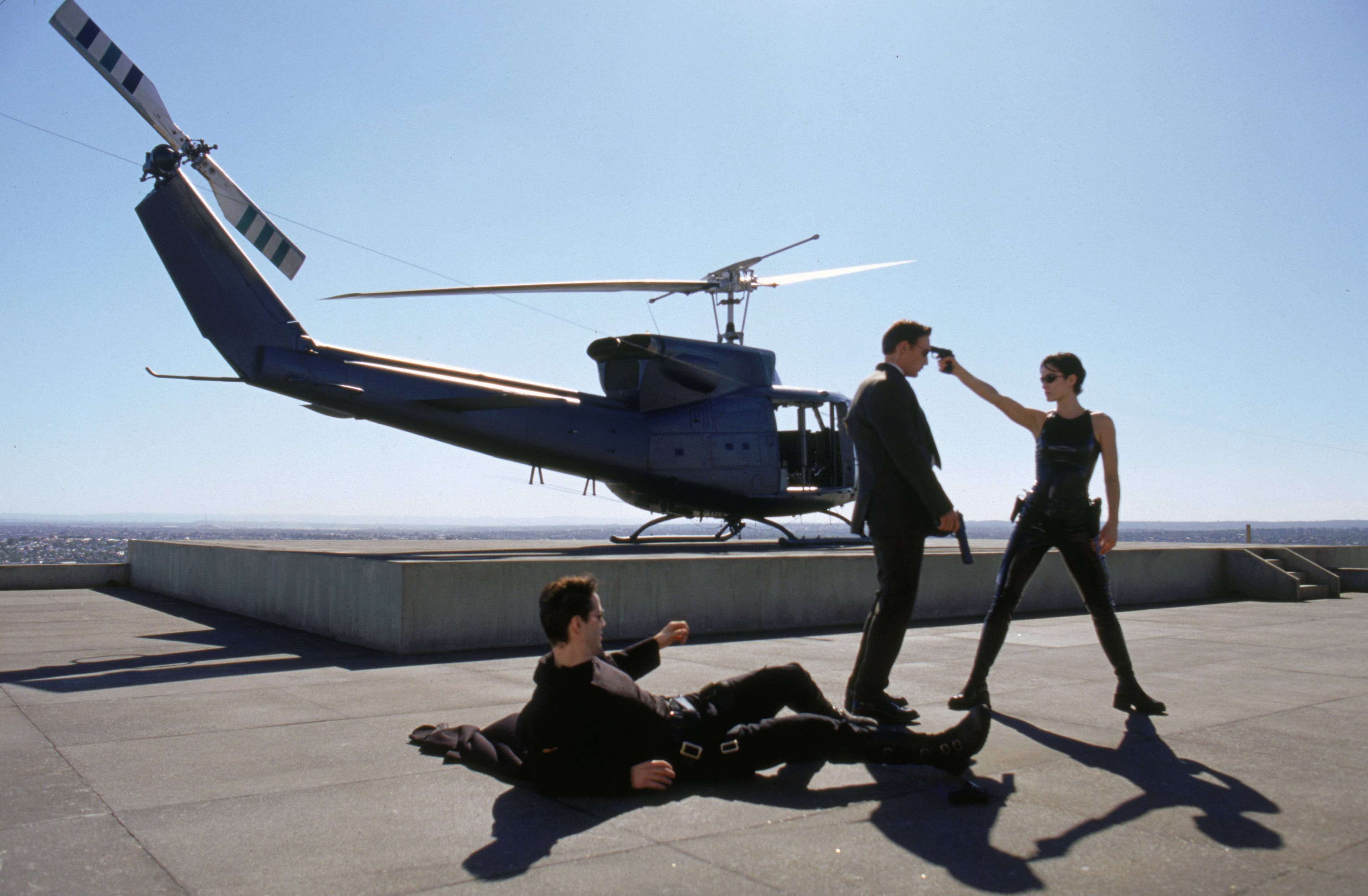 Behind-the-scenes image of the rooftop action setup with helicopter, cast, and crew visible.