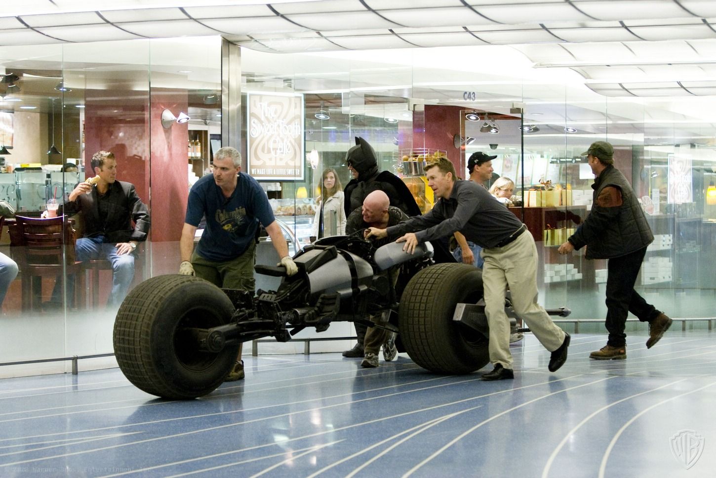 Behind-the-scenes image of crew moving or preparing the Bat vehicle on a bright interior set.