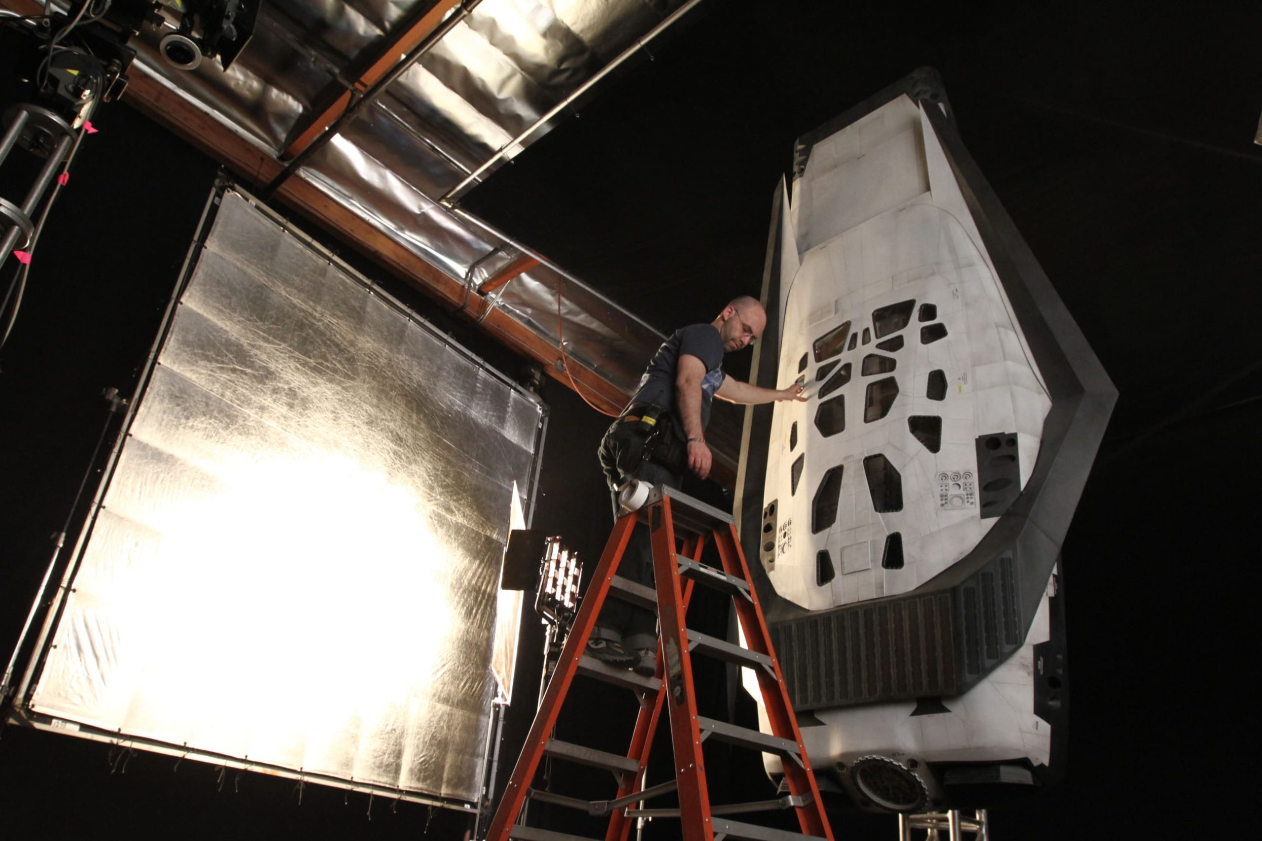 Behind-the-scenes image of crew lighting or preparing a spacecraft shell on set.